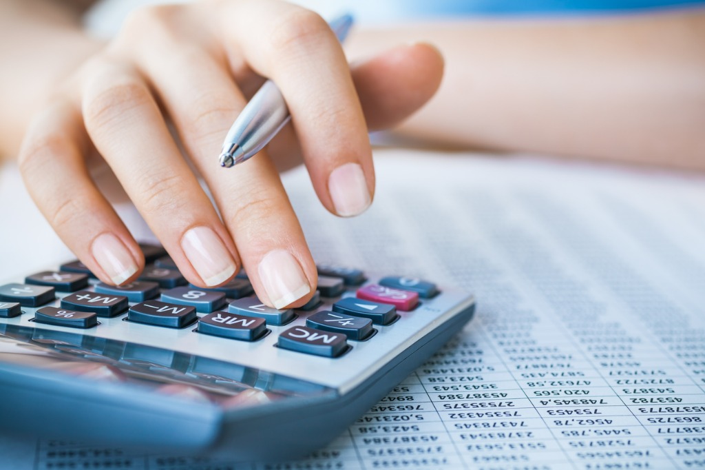 Woman's hand holding a pen while using a calculator, finance sheet sitting under the calculator