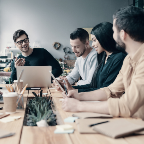 four people sitting around the table. Person at the head of the table speaking 